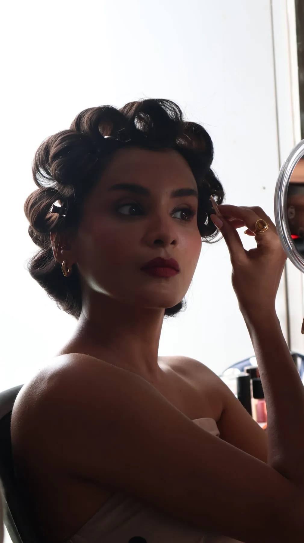 Disha Pardeshi in hair rollers checking her make-up in a hand mirror before the shoot