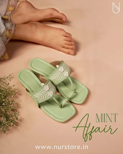 Pair of mint green sandals on a peach background beside bare feet and dried flowers