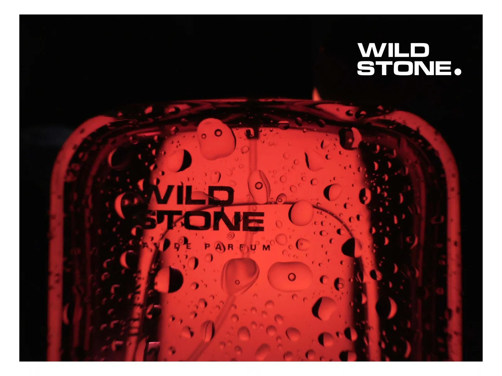 Wild Stone eau de parfum bottle lit in deep red, covered in water droplets against black